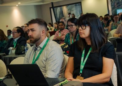 Two DNSG 2026 attendees listening to a scientific presentation with a laptop on the table.