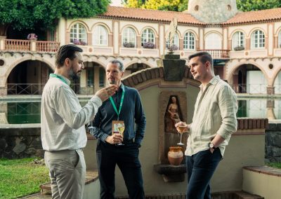 Three symposium attendees talking over drinks beside a fountain in the venue courtyard.
